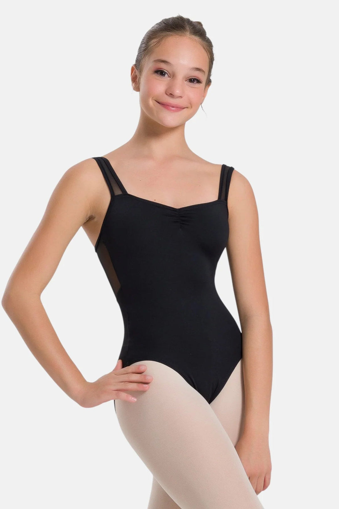 A young dancer wearing a black bodysuit with sheer mesh side panels and beige tights, posing against a light gray studio background.