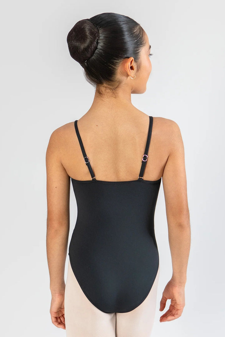 A young gymnast or dancer shown from the back, wearing a black leotard with thin shoulder straps and light beige tights, against a plain light gray studio background.